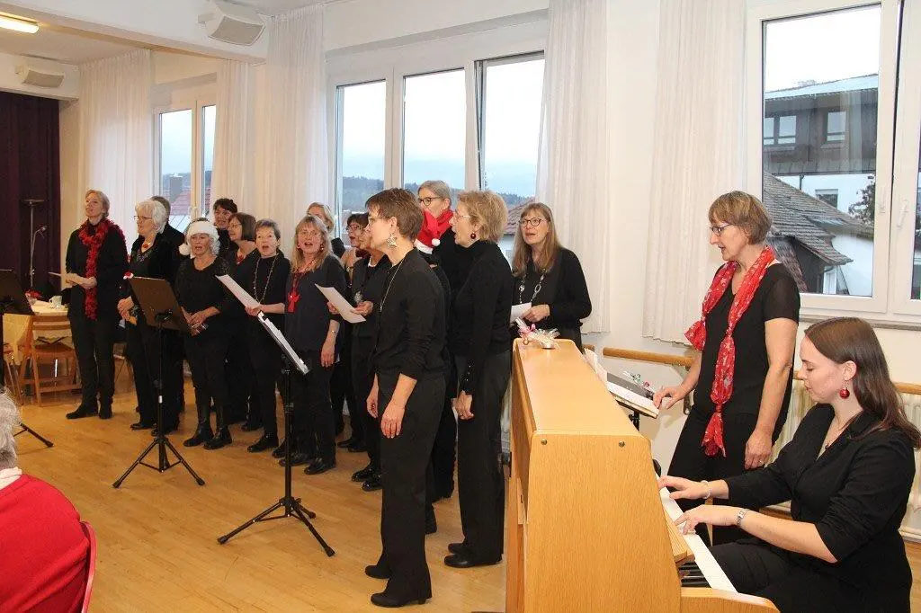 Adventskonzert: Der Frauenchor PopUp singt vor großen Fenstern, im Vordergrund Anna-Luisa Kächele am Klavier.