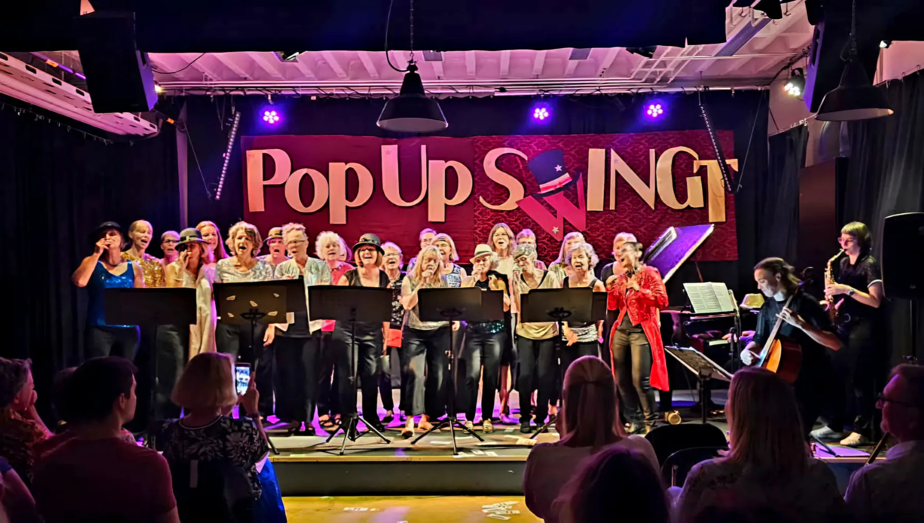 Der Frauenchor PopUp auf der PopUpSwing-Bühne mit Banner und Saxophon-Begleitung.